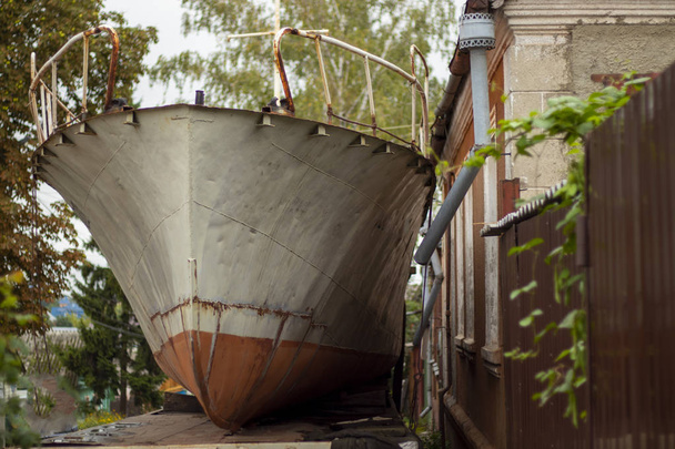 een oud roestig schip staat geparkeerd in de buurt van een huis in de stad Koersk Rusland in de herfst - Foto, afbeelding
