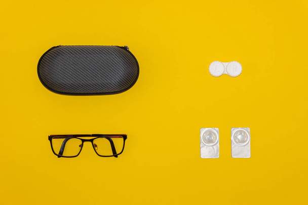 Gafas, lentes de contacto y estuches de almacenamiento sobre fondo amarillo
 - Foto, Imagen