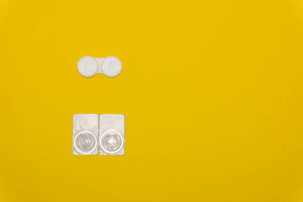 Lentes de contacto y estuche de almacenamiento de lentes sobre fondo amarillo
 - Foto, Imagen