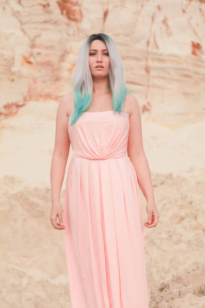 Fiatal gyönyörű kaukázusi nő, hosszú rózsaszín ruhában pózol a sivatagi táj homokkal. - Fotó, kép