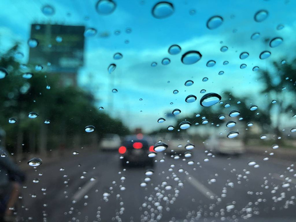 car windshield with raindrops on blurred street background with traffic in city at rainy day - Фото, изображение