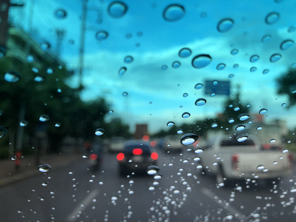 car windshield with raindrops on blurred street background with traffic in city at rainy day - Photo, Image