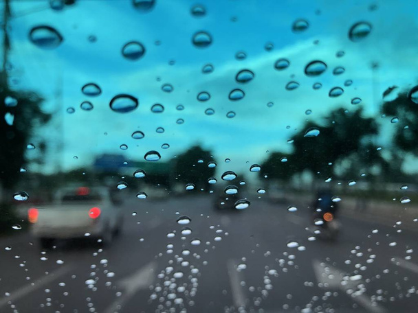 car windshield with raindrops on blurred street background with traffic in city at rainy day - Fotoğraf, Görsel