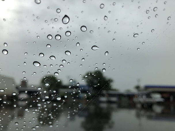 pare-brise de voiture avec gouttes de pluie sur fond de rue floue avec la circulation en ville le jour de pluie
 - Photo, image