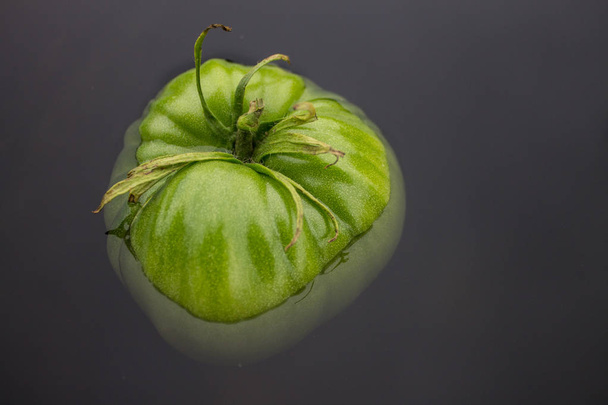 Large green tomato floating in dark water - Fotoğraf, Görsel