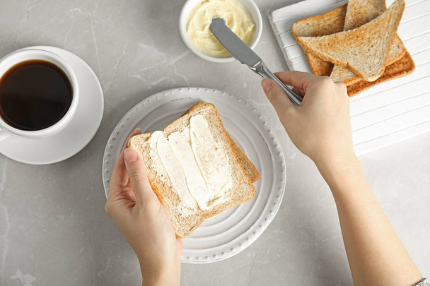 Woman spreading butter onto slice of bread over grey table, top view - Fotografie, Obrázek