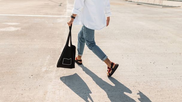 Young man in fashionable summer clothes in stylish red sandals with a black vintage bag runs down the street. Close-up male legs. Trendy mens clothing. Stylish look. - Foto, Imagen