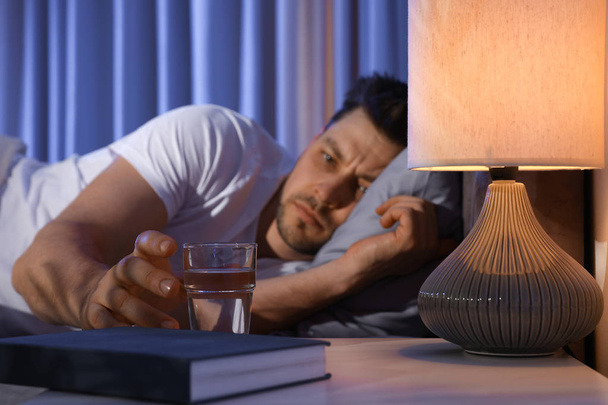 Sleepy man reaching for glass of water in dark room at night. Bedtime - Zdjęcie, obraz