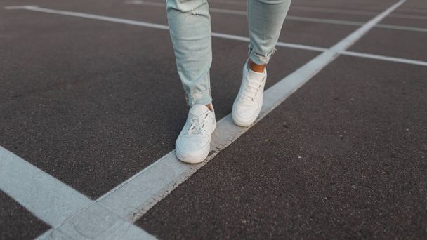 Fashionable men's white leather white sneakers. Stylish men's shoes. Casual design. Closeup of male legs in blue jeans and trendy footwear. Summer style. - Photo, image