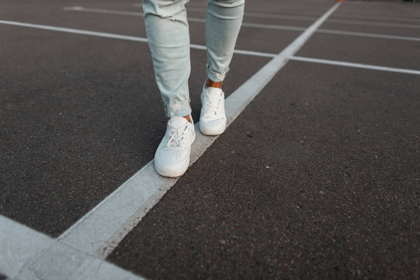 trendiger junger Mann in weißen Lederturnschuhen in modischer blauer Jeanshose. stylische Sommerschuhe für Männer. Casual Design. Nahaufnahme männlicher Beine. - Foto, Bild