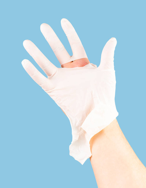 gebrochene weiße Latex-Chirurgenhandschuh auf kaukasischer Hand isoliert auf blauem einfarbigem Hintergrund - Foto, Bild