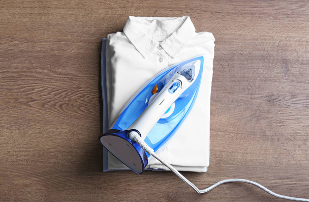 Flat lay composition with folded clothes and iron on wooden table - 写真・画像
