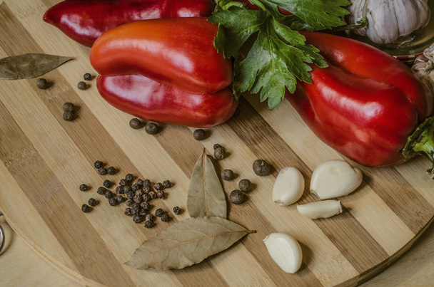 Cutting board with red pepper with celery leaves, bay leaves,garlic and allspice - Foto, Imagem