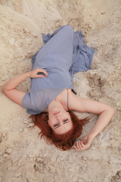 Νέα όμορφη καυκάσιος γυναίκα σε γκρίζο φόρεμα σιφόν που βρίσκεται σε έρημο τοπίο με άμμο. - Φωτογραφία, εικόνα