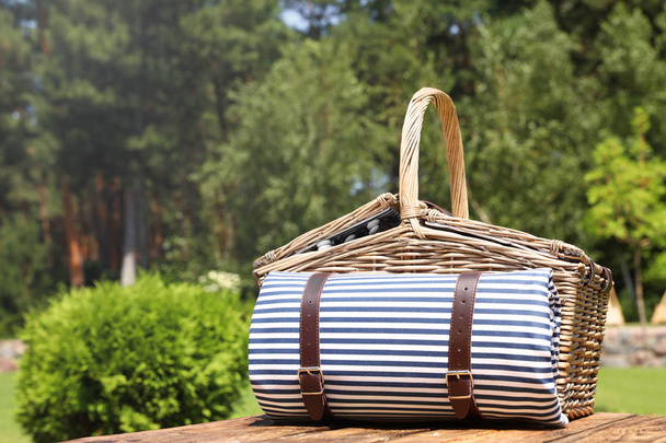 Picnic basket with blanket on wooden table in garden - Fotó, kép