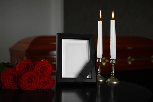Black photo frame with burning candles and red roses on table in funeral home - Fotografie, Obrázek