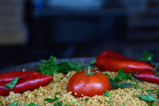 Σε ένα τηγάνι από χυτοσίδηρο, πιλάφι διακοσμημένο με κόκκινο πιπέρι, ντομάτες, βότανα, μαϊντανό. Η ιδέα είναι ένα δείπνο διακοπών. Γιορτάκι. Ασιατική κουζίνα - Φωτογραφία, εικόνα