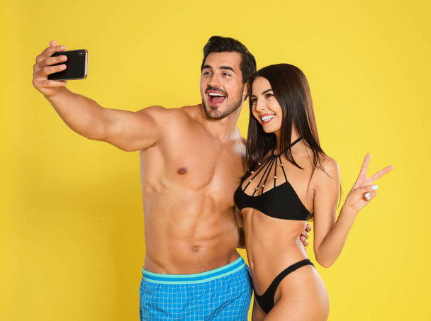 Young attractive couple in beachwear taking selfie on yellow background - 写真・画像