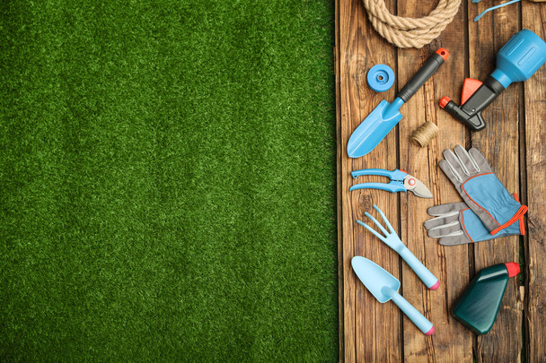Superfície de madeira com ferramentas de jardinagem na grama verde, leigos planos. Espaço para texto
 - Foto, Imagem
