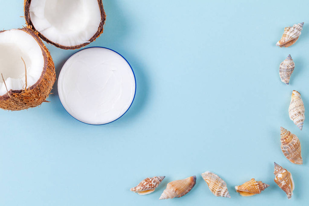 Halves of chopped coconut on blue background with seashells and cream jar - Foto, imagen