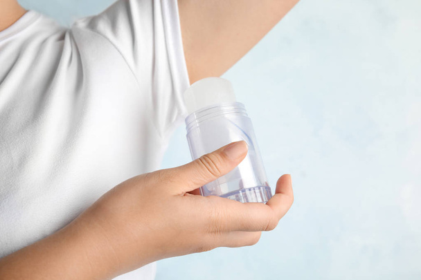 Young woman holding natural crystal alum deodorant near armpit on light blue background, closeup - Photo, image