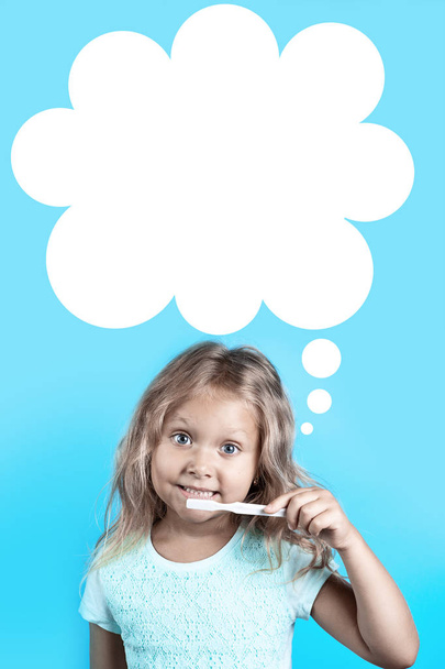 Cute girl with curly hair brush her teeth with white toothbrush on a blue background. - Foto, Imagem