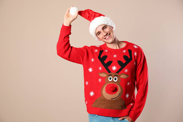 Portrait of young man in Christmas sweater and Santa hat on beige background - Zdjęcie, obraz