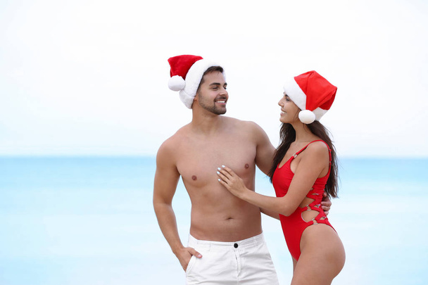 Happy young couple with Santa hats together on beach - Φωτογραφία, εικόνα