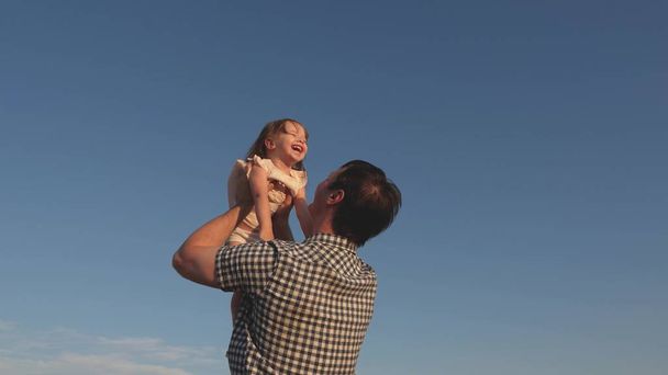 父は青い空に幸せな娘を投げ出す。父と小さな子供の遊び、笑いと抱擁を一緒に。幸せな家族旅行。親の腕の中で赤ちゃん。お父さん休み。幸せな家庭の概念. - 写真・画像