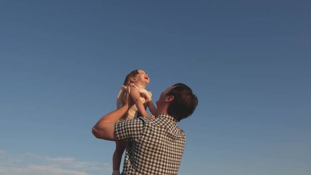 Apa feldob egy boldog lányt a kék égre. Apa és a kisgyerek együtt játszanak, nevetnek és ölelkeznek. Boldog családi utazást. Baba a szülő karjaiban. Apa szabadnapja. A boldog család fogalma. - Fotó, kép