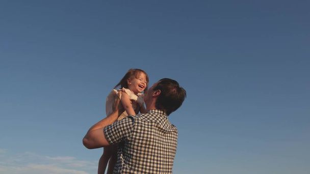 Tata wymiotuje szczęśliwą córką na niebieskim niebie. Ojciec i małe dziecko bawią się, śmieją się i przytulają. Szczęśliwej podróży rodzinnej. Dziecko w ramionach rodzica. Dzień wolny od taty. Koncepcja szczęśliwej rodziny. - Zdjęcie, obraz