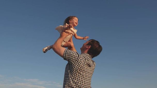 Papa wirft eine glückliche Tochter in den blauen Himmel. Vater und Kind spielen, lachen und umarmen sich. Glückliche Familienreisen. Baby in den Armen der Eltern. Vatertag frei. Das Konzept einer glücklichen Familie. - Foto, Bild
