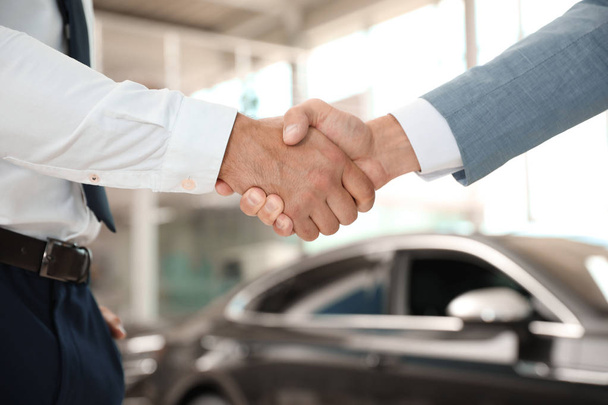 Young salesman shaking hands with client in modern car dealership, closeup - Φωτογραφία, εικόνα