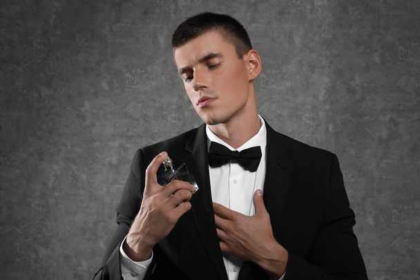 Handsome young man using perfume on grey stone background - Zdjęcie, obraz