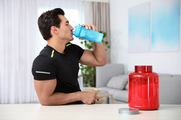 Young athletic man drinking protein shake at home - Fotó, kép