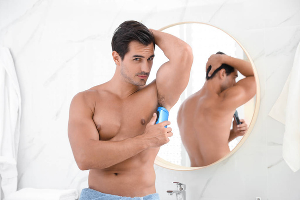 Handsome young man applying deodorant in bathroom - 写真・画像
