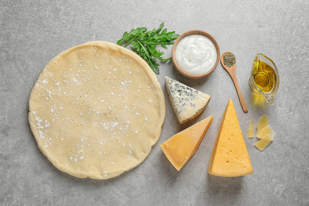 Flat lay composition with pizza crust and fresh ingredients on grey table - Fotoğraf, Görsel