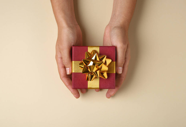 Woman holding beautiful gift box on beige background, top view - 写真・画像