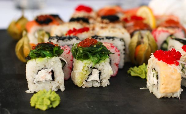 Conjunto de rolos de sushi com vasabi e gengibre em uma placa de ardósia escura, mesa de bufete, orientação horizontal, close-up
 - Foto, Imagem