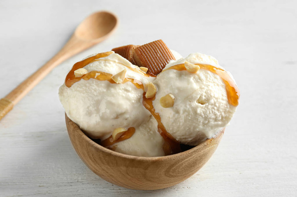 Delicious ice cream with caramel candies in bowl on white wooden table - Фото, изображение