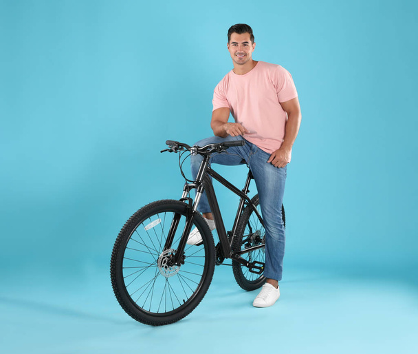 Handsome young man with modern bicycle on light blue background - Fotografie, Obrázek