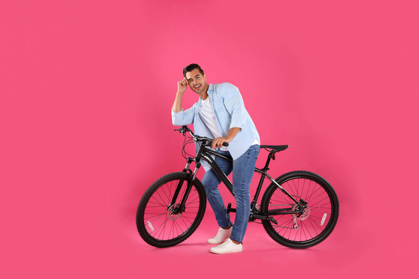 Handsome young man with modern bicycle on pink background - Photo, Image