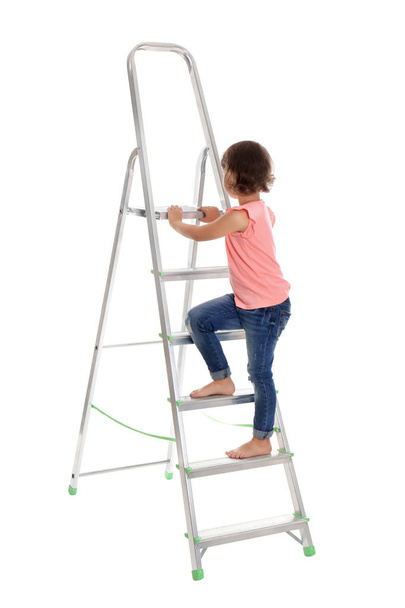 Ένα κοριτσάκι που σκαρφαλώνει στην σκάλα σε λευκό φόντο. Κίνδυνος στο σπίτι - Φωτογραφία, εικόνα