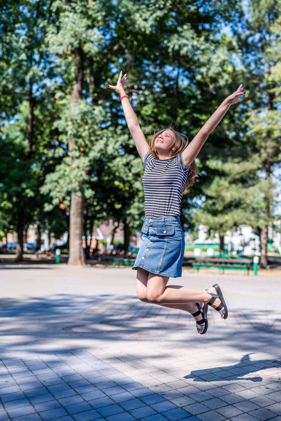 Ευτυχισμένη καυκάσιος γυναίκα σε casual ρούχα χαμογελώντας πηδώντας στο πάρκο το καλοκαίρι ηλιόλουστη μέρα - Φωτογραφία, εικόνα