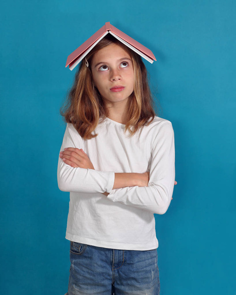 Little girl with a book on her head with an angry expression - Фото, зображення