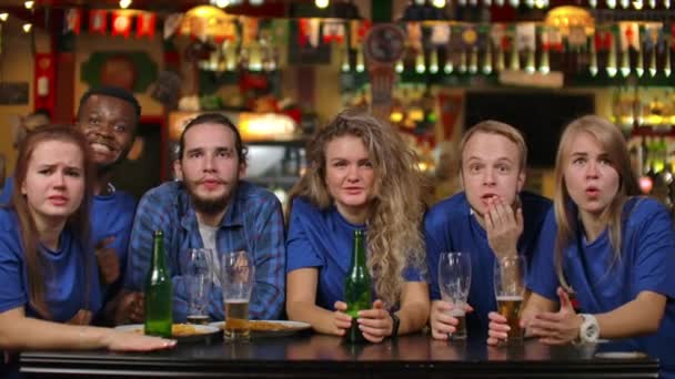 A group of young people watching the broadcast of a sporting event on TV in a beer bar, emotionally waiting for a decisive moment and feeling sad after losing a team - Footage, Video