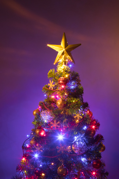 Kerstboom met feestelijke verlichting, paarse achtergrond - Foto, afbeelding