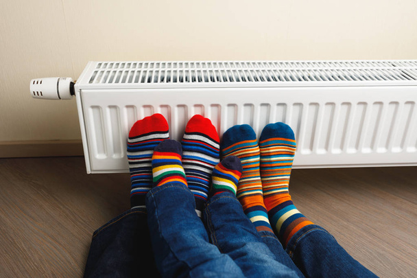 pernas com meias coloridas na frente do radiador de aquecimento
 - Foto, Imagem