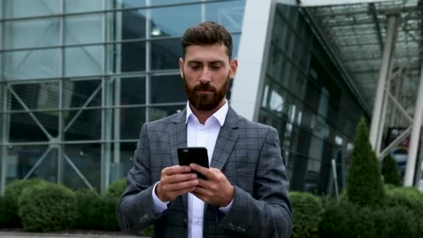 Businessman using smartphone and smiling at airport. Young business executive with mobile phone at airport. - Materiał filmowy, wideo