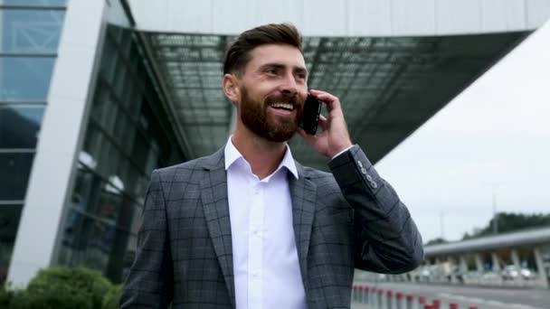 Business, technology and people concept - smiling businessman with smartphone talking over office building - Materiał filmowy, wideo
